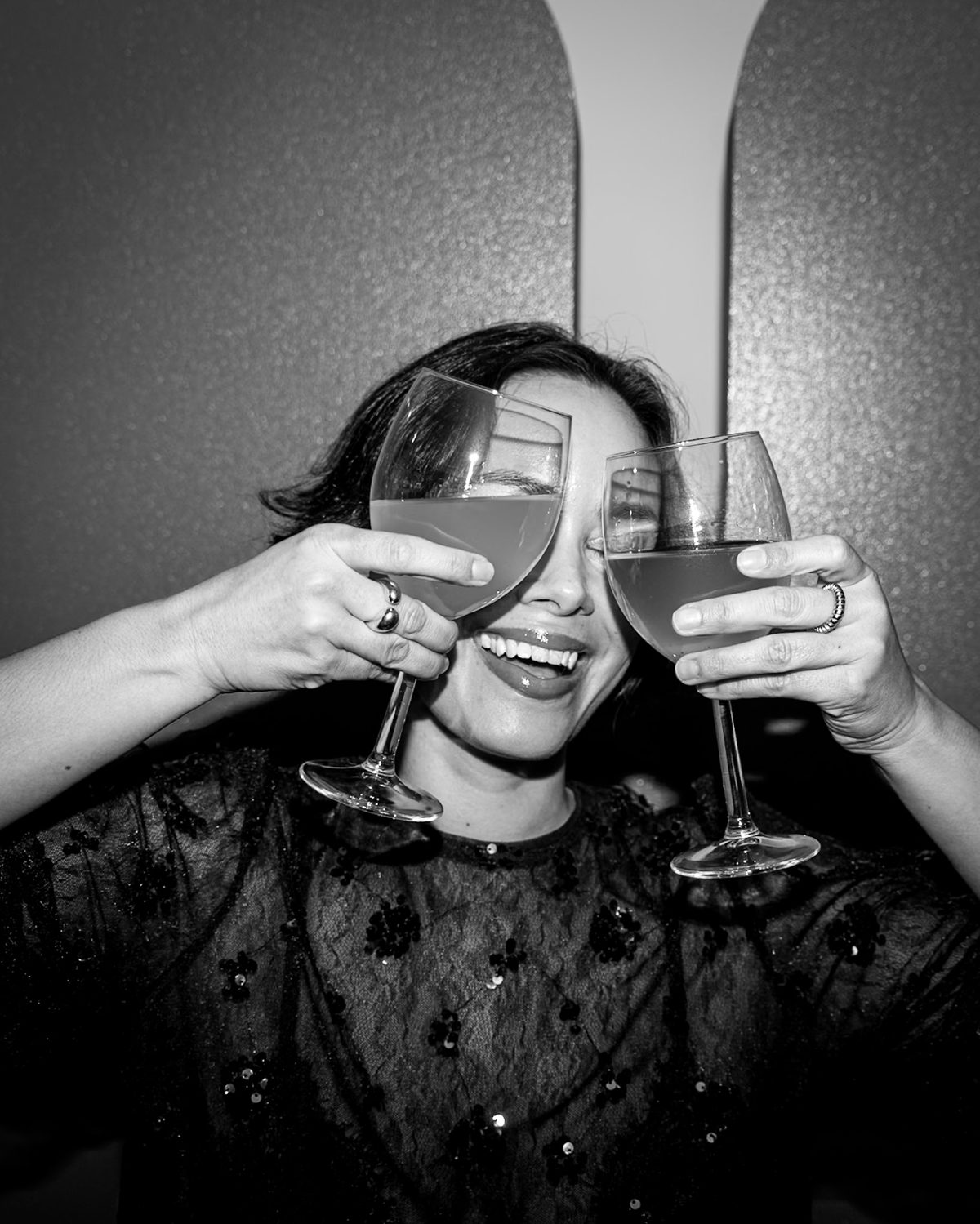 Laughing guest holding two wine glasses over her eyes at an event