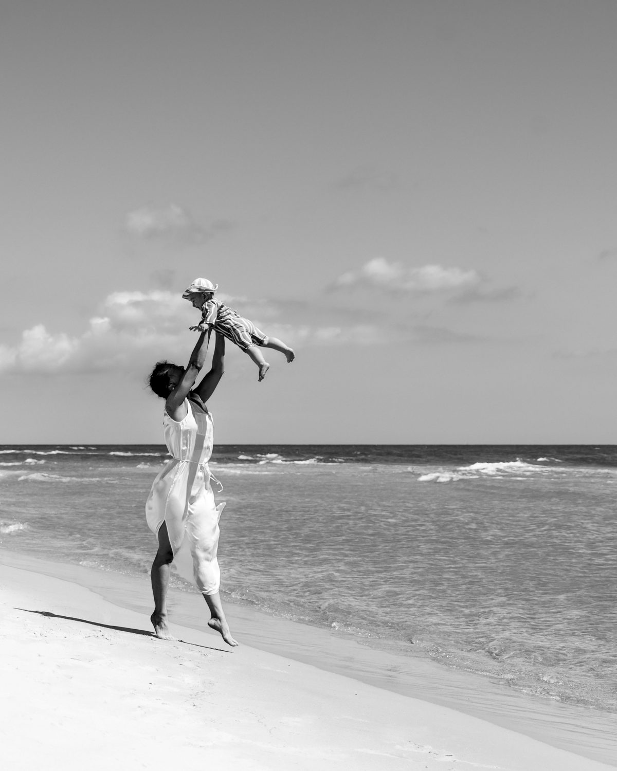 Mother lifting her baby into the air on a sunny beach