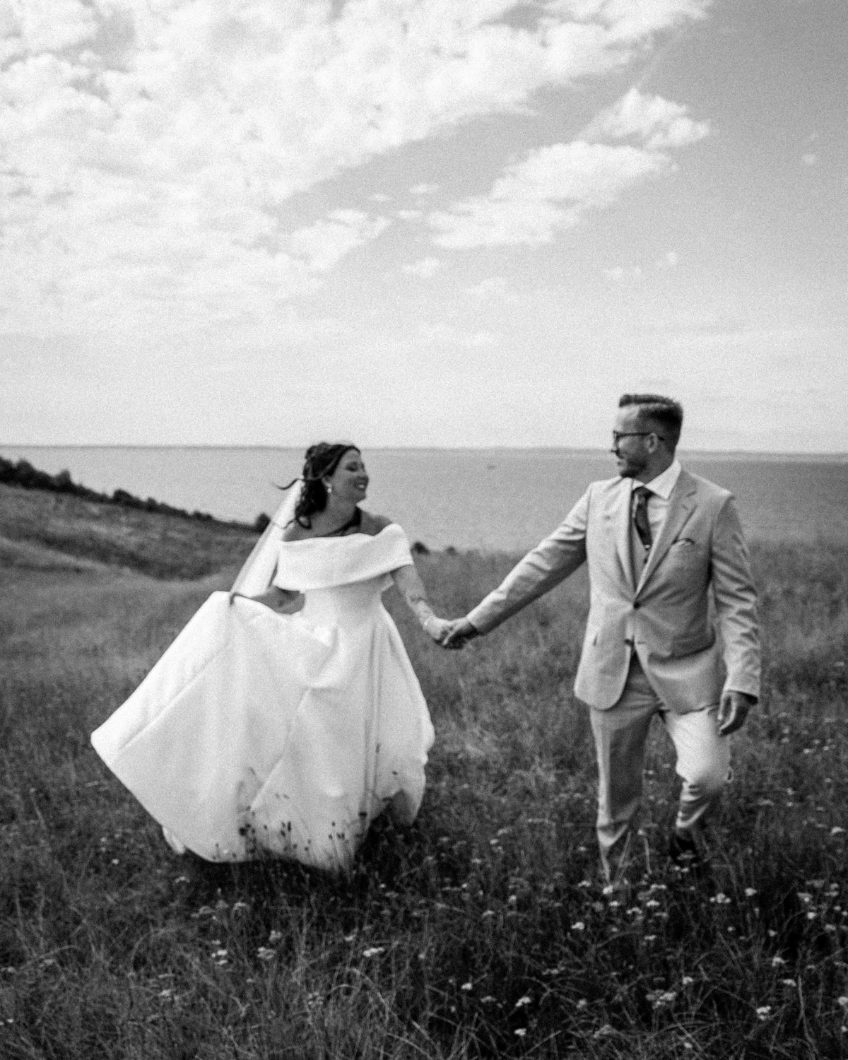 Bride and groom walking hand in hand through a meadow by the sea