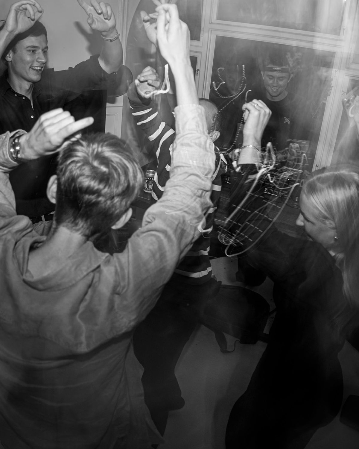 Colleagues dancing with their hands in the air around a DJ at an office party